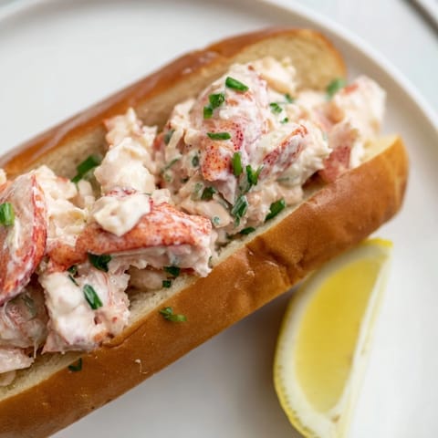 A close-up of a classic New England Lobster Roll brimming with juicy lobster and fresh chives.