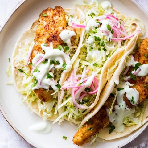 A platter of freshly assembled fish tacos with vibrant slaw and drizzled sauce for a coastal-inspired meal.