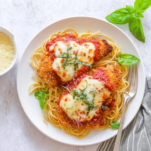 Juicy Chicken Parmesan baked until bubbly and served over al dente pasta, garnished with fresh basil leaves.
