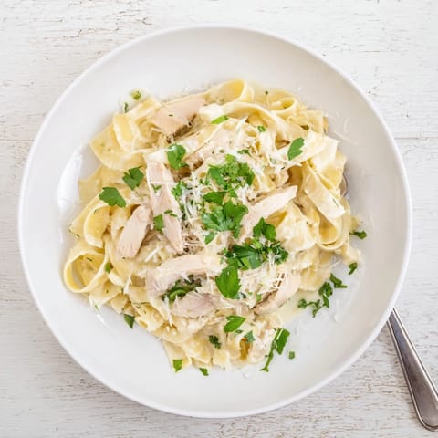 A close-up of Fettuccine Alfredo showing silky noodles coated in buttery sauce, topped with sliced chicken.