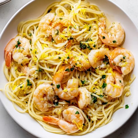 Shrimp glistens with buttery lemon garlic sauce over spaghetti in a rustic skillet.  