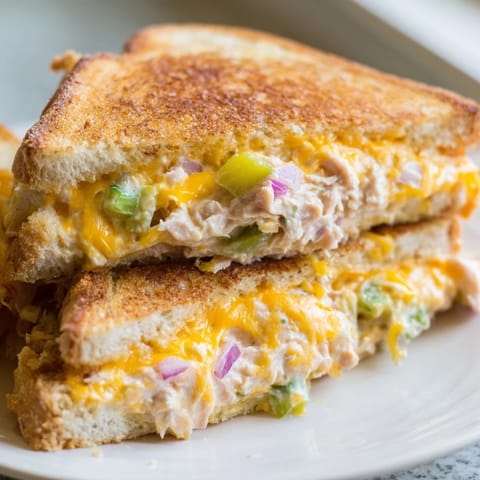 Melted cheddar and spicy tuna salad spill from a buttery, grilled sourdough sandwich, cut diagonally.