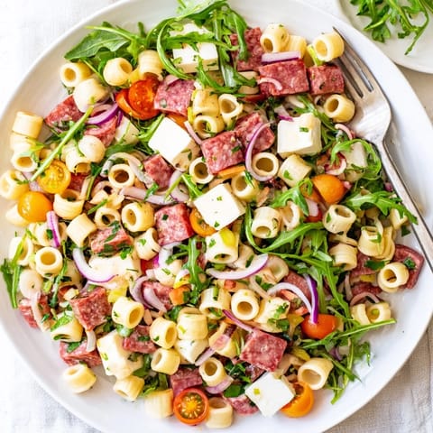 A vibrant bowl of Spring Antipasto Pasta Salad with ditalini, arugula, salami, and mozzarella pearls, tossed in a zesty dressing.