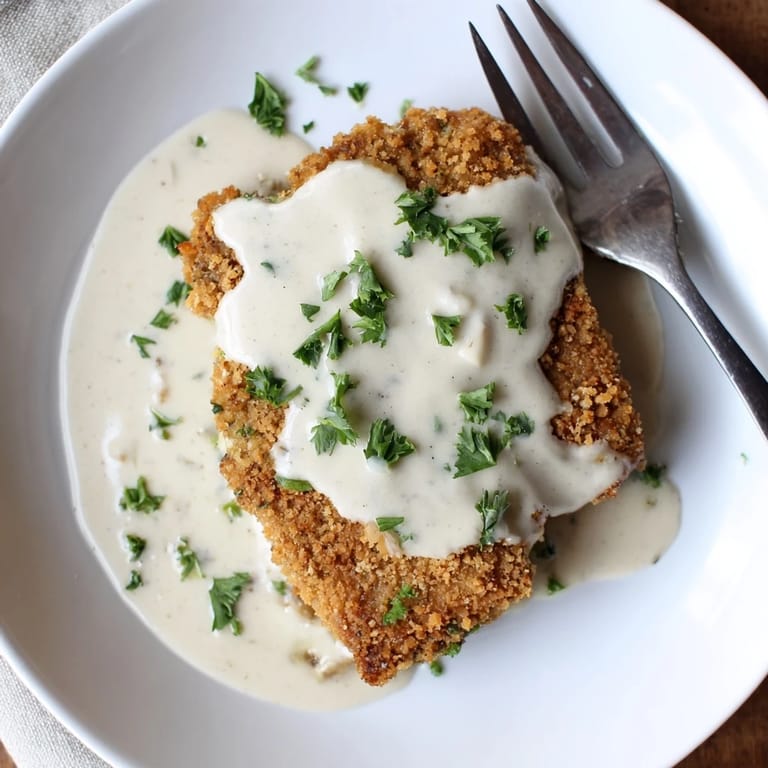 Close up of crispy Chicken Fried Steak drizzled with creamy gravy, showing juicy steak through the crunchy coating.