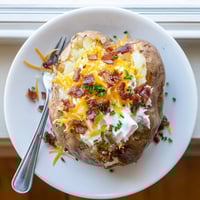 Golden brown baked russet potatoes are loaded with butter, sour cream, sharp cheddar, and crispy bacon crumbles topped with fresh green chives.
