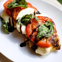 Golden-brown Caprese Chicken Skillet with melted mozzarella and fresh basil leaves on a rustic wooden table.  