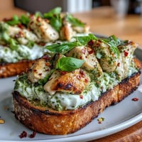 Crisp sourdough toast topped with pesto, tender chicken, and creamy burrata garnished with fresh basil.  