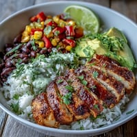 Golden-brown Cajun chicken slices rest on fluffy white rice, surrounded by sweet corn, black beans, and diced red and yellow peppers.