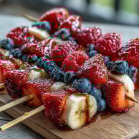 Festive Fourth of July fruit skewers with strawberries, bananas, and blueberries on a white platter.